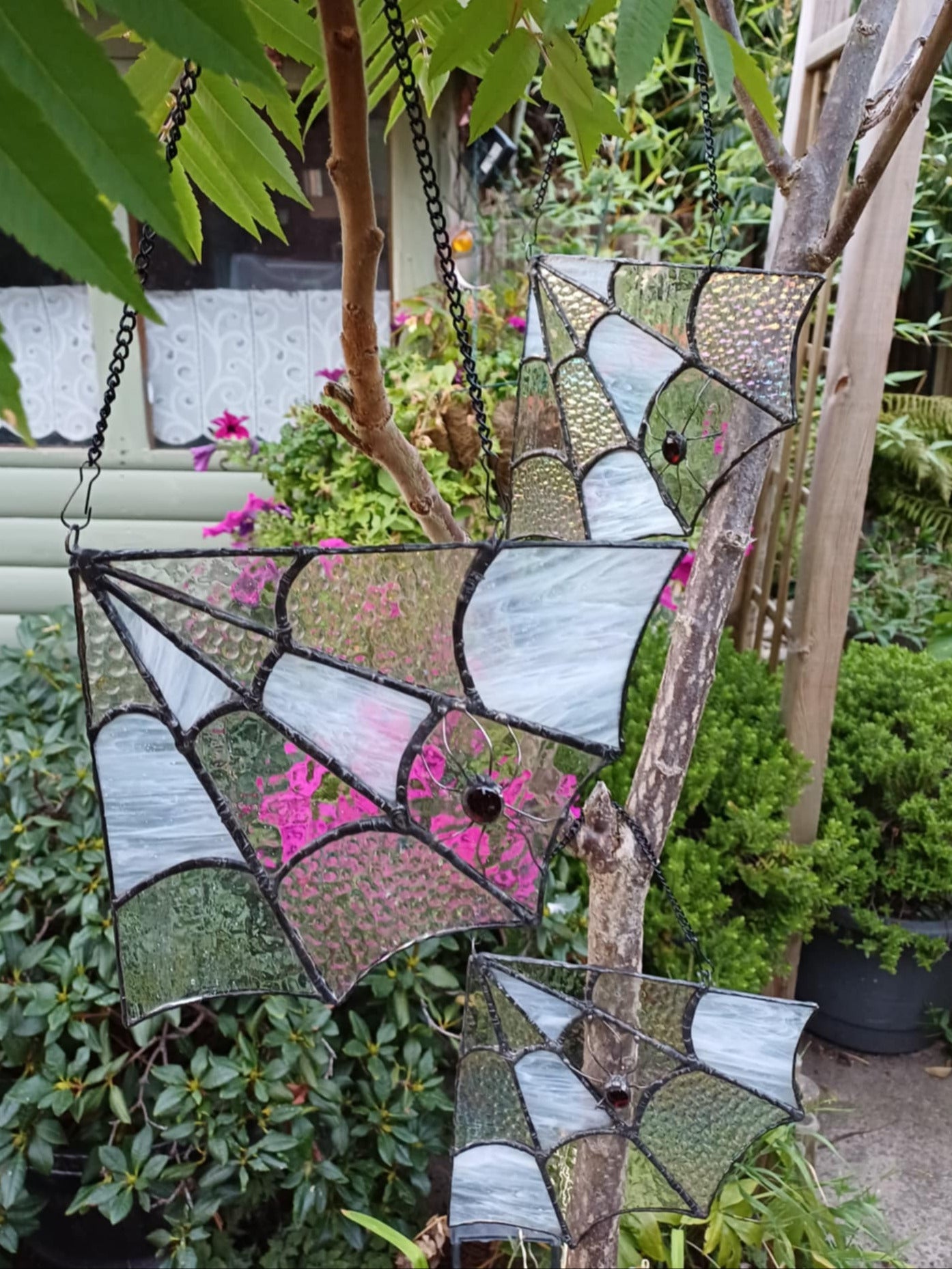 3 Stained glass webs hanging on a tree branch with a garden background